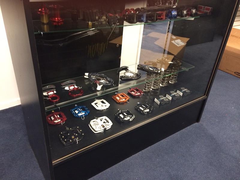 Display case filled with various bicycle components, including colorful pedals and gears arranged neatly on glass shelves in a retail setting.