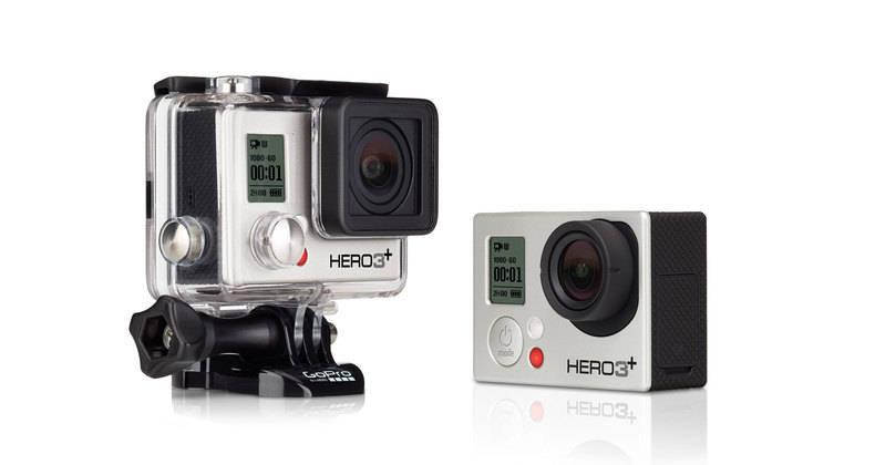 GoPro Hero 3 Plus: Two GoPro cameras side by side: the left camera is in a protective case with a transparent front and has a digital display showing recording time, while the right camera is compact and features a simplified design with a larger lens and red recording button. Both are labeled as HERO3+.