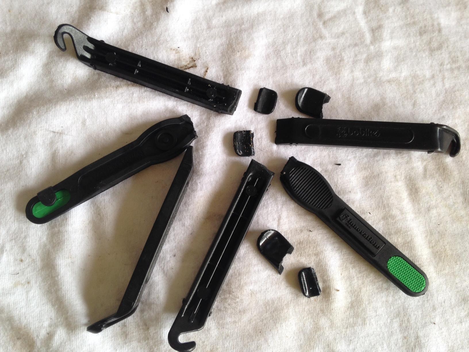WTB Bronson 2.2 29er: A collection of black bicycle tire levers, some intact and some broken, arranged on a light-colored cloth surface. The tools are designed for removing and installing tires on bicycles.