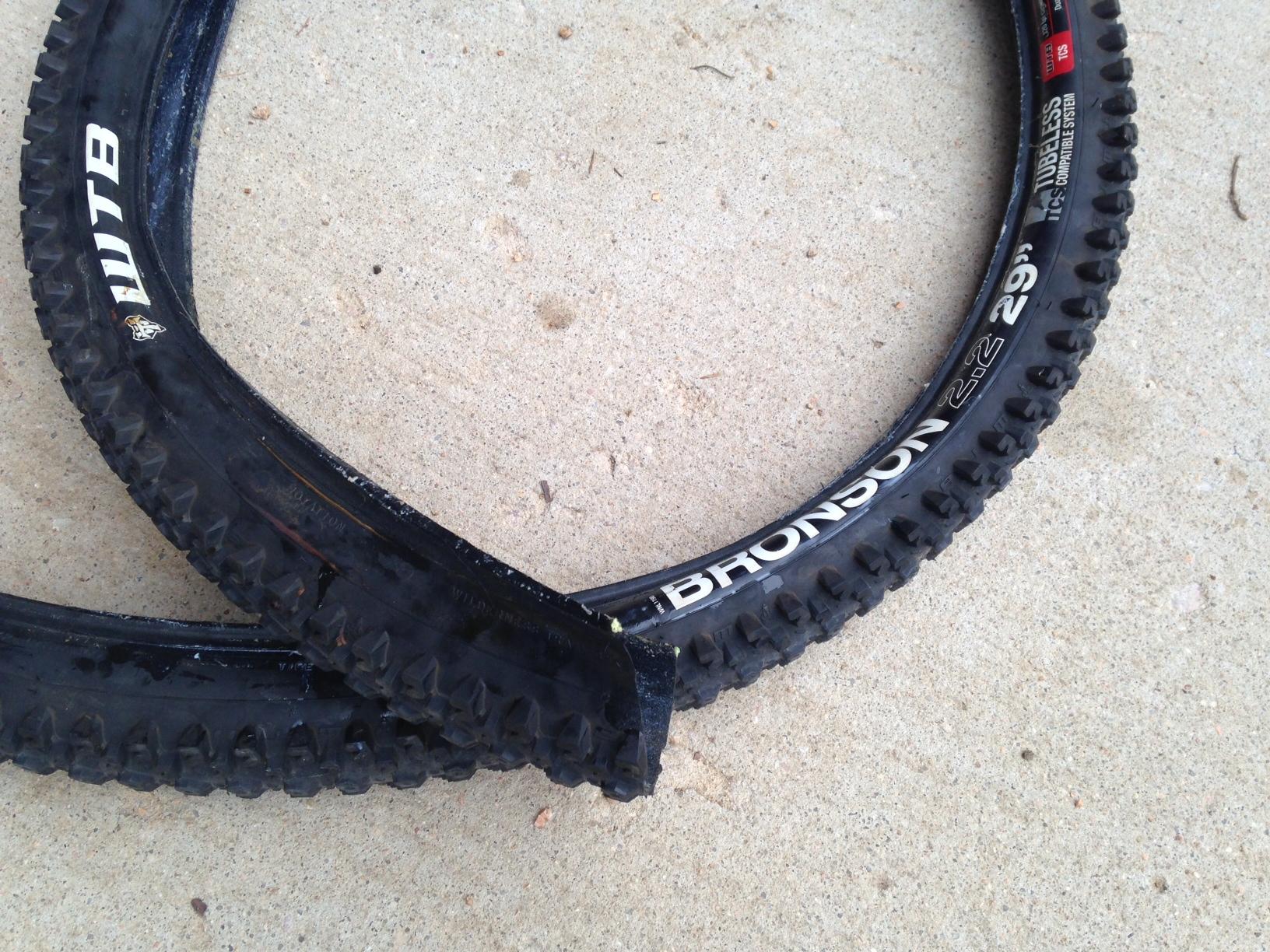 WTB Bronson 2.2 29er: Two mountain bike tires lying on a concrete surface. One tire is partially sliced, showing the inner structure, while the other tire remains intact. The visible branding includes "WTB" and "Bronson 29" on the sidewalls.