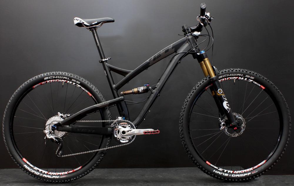 Yeti SB95: Mountain bike displayed against a dark background, featuring a sleek black frame, front suspension fork, and knobby tires. The bike is equipped with high-performance components, including a cassette and chain assembly, and has a modern, aerodynamic design suitable for off-road cycling.