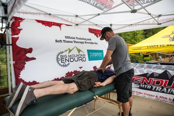 A person receiving soft tissue therapy on a massage table under a tent, with branding for Big Mountain Enduro and Yeti visible in the background. Keystone Resort Bike Park mountain bike trail.