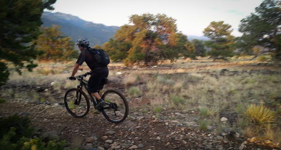 A person riding a mountain bike on a rocky trail in a natural outdoor setting with trees and mountains in the background during the evening. Methodist Mountain mountain bike trail.