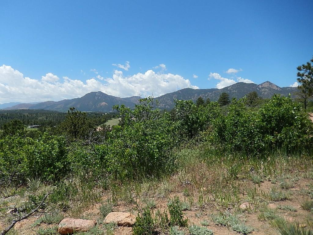 A scenic mountainous landscape under a blue sky with scattered clouds, featuring lush greenery in the foreground and trees scattered throughout the view, showcasing a peaceful natural setting. Falcon Trail mountain bike trail.