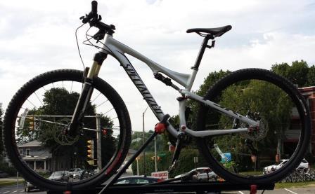 Specialized Epic Comp 29er: A white mountain bike mounted on a bike rack, with a blurred background showing traffic lights and greenery.