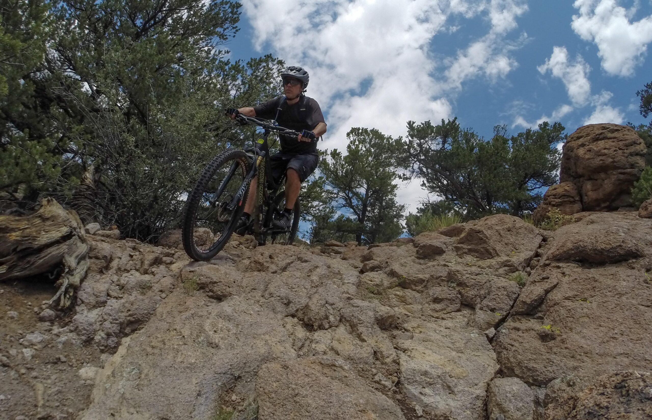 A person riding a mountain bike on a rocky trail surrounded by trees under a partly cloudy sky. Unkle Nazty mountain bike trail.