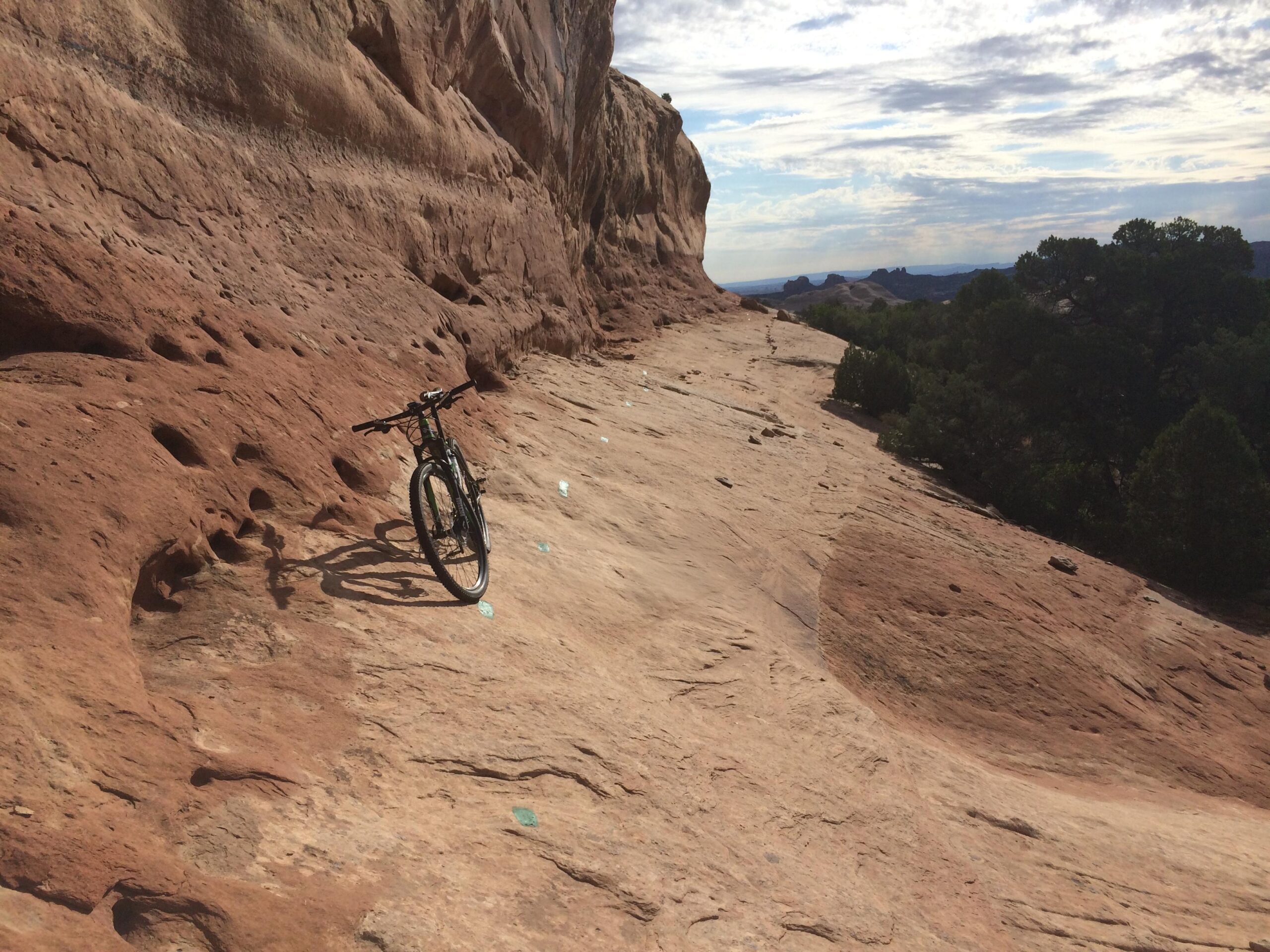 A mountain bike resting on a rocky pathway surrounded by a red sandstone landscape, with distant hills and a partly cloudy sky in the background. Navajo Rocks mountain bike trail.