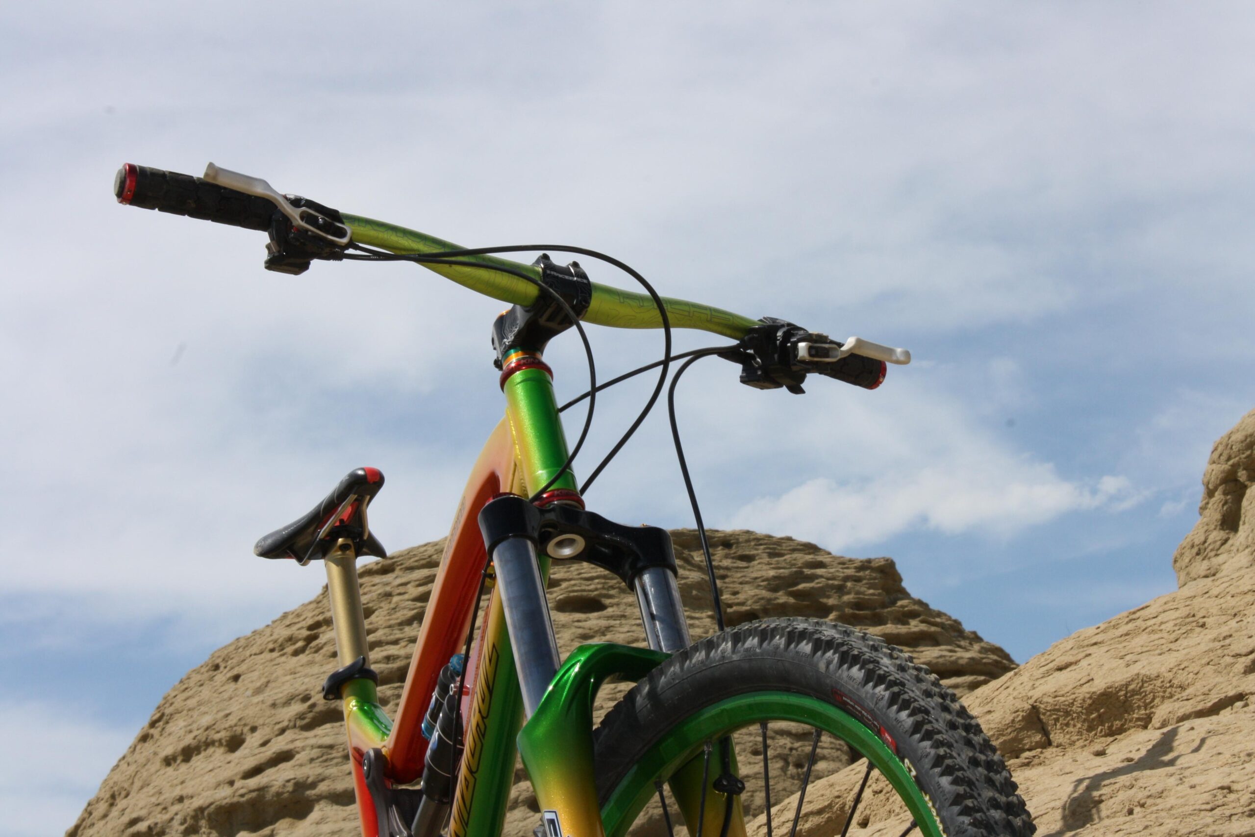 Santa Cruz Nomad: Mountain bike with colorful handlebars and frame, positioned against a rocky landscape under a cloudy sky.
