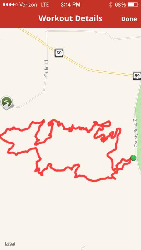 A red GPS workout route displayed on a mobile app, depicting a winding path through an area with minimal roads and features. The route showcases various twists and turns, representing an outdoor activity. The background includes a vague map with road labels and connectivity icons. Emma Carlin mountain bike trail.