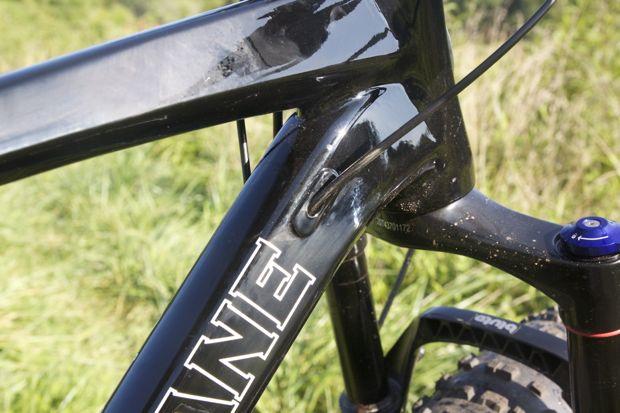 Motobecane NightTrain Bullet: Close-up view of a black bicycle frame showing the bottom bracket area, with visible details of the tubing and cable routing against a backdrop of green grass.