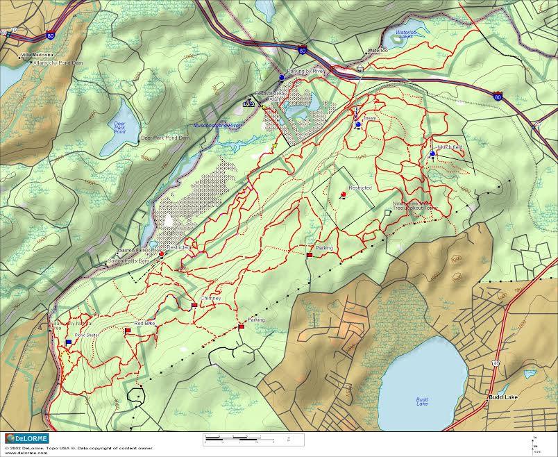 A detailed topographic map showing trails and paths in a natural area, featuring marked parking locations, roadways, and nearby water bodies. The map includes contour lines indicating elevation changes and highlights various points of interest within the park or recreation area. Allamuchy North-Deer Park-Stephens Connecter Ride mountain bike trail.