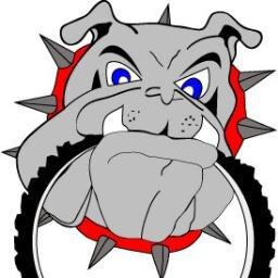 A graphic illustration of an angry-looking bulldog with blue eyes, displaying prominent teeth and spikes on its collar. The bulldog is holding a bicycle tire in its mouth, set against a bold, circular background.