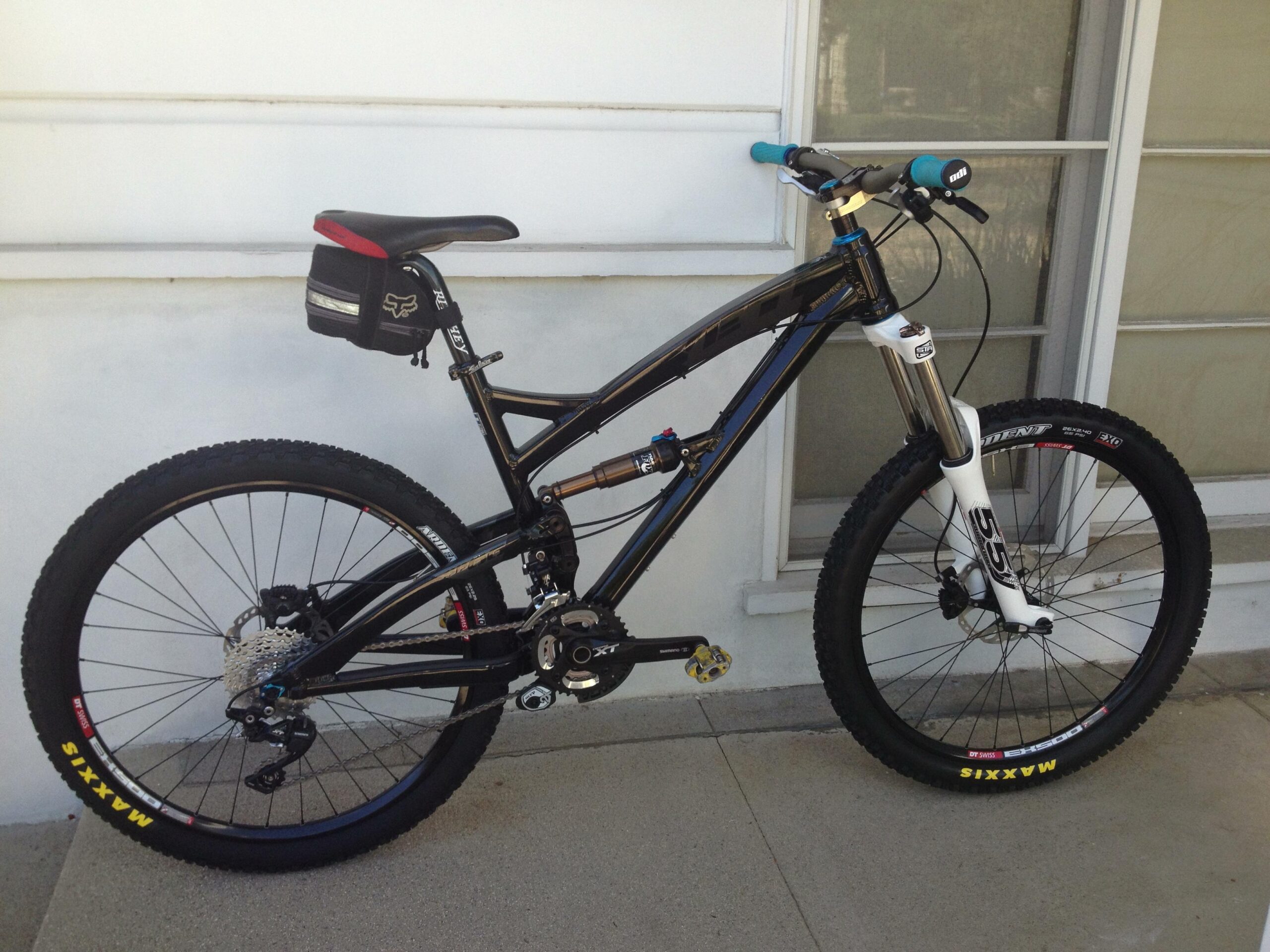 Yeti SB66: A black and blue mountain bike with a white front fork, equipped with knobby tires and a small black saddle bag. The bike is positioned against a light-colored wall.