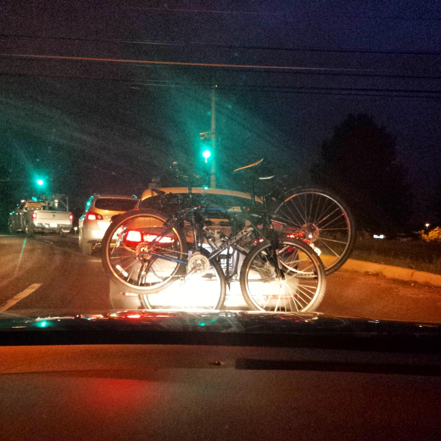Trek 4500: A view from inside a car showing bicycles mounted on the back of another vehicle, with a green traffic light ahead in a nighttime setting.