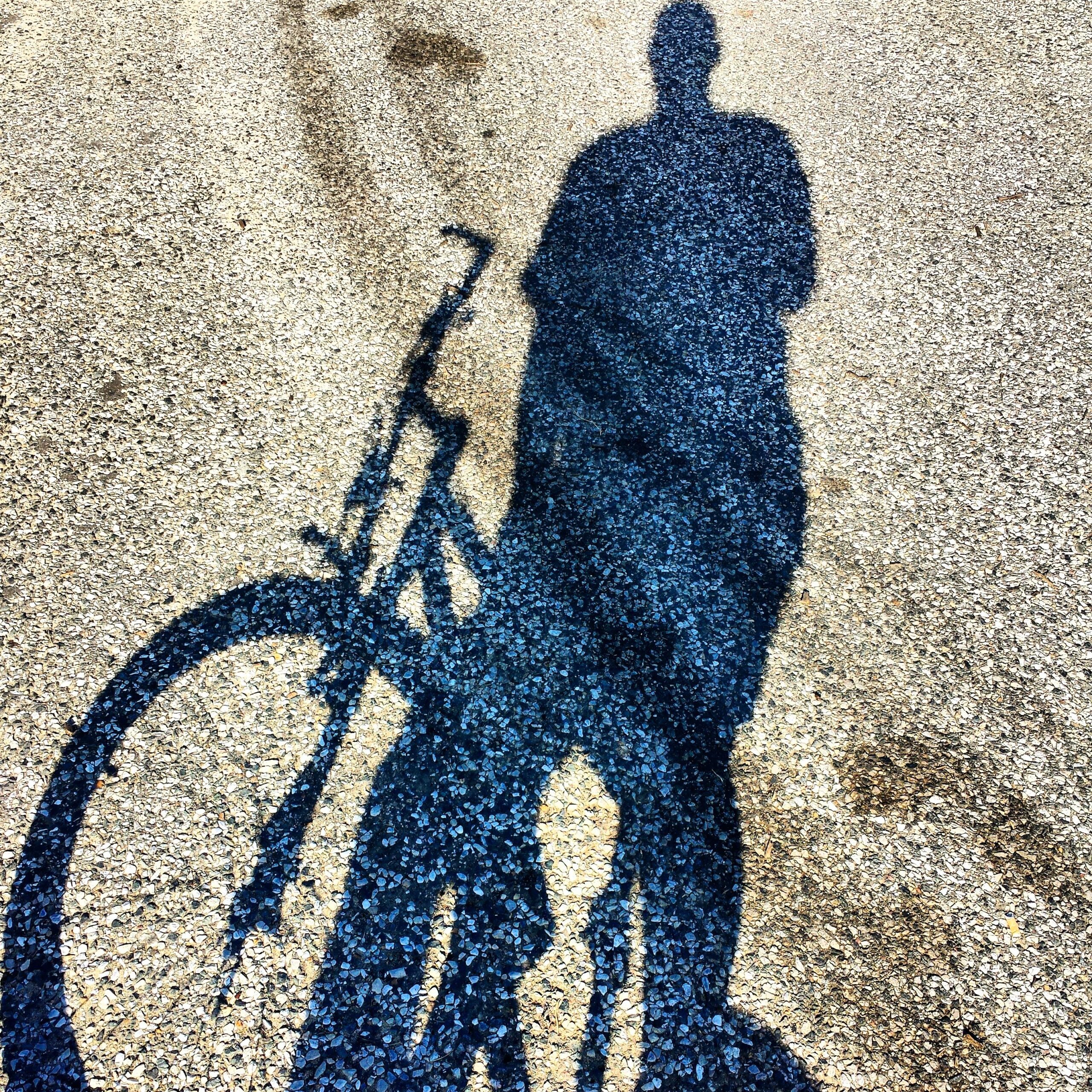 Trek 4500: Shadow of a person standing next to a bicycle on a gravel surface, with sunlight casting distinct outlines of both the figure and the bike.