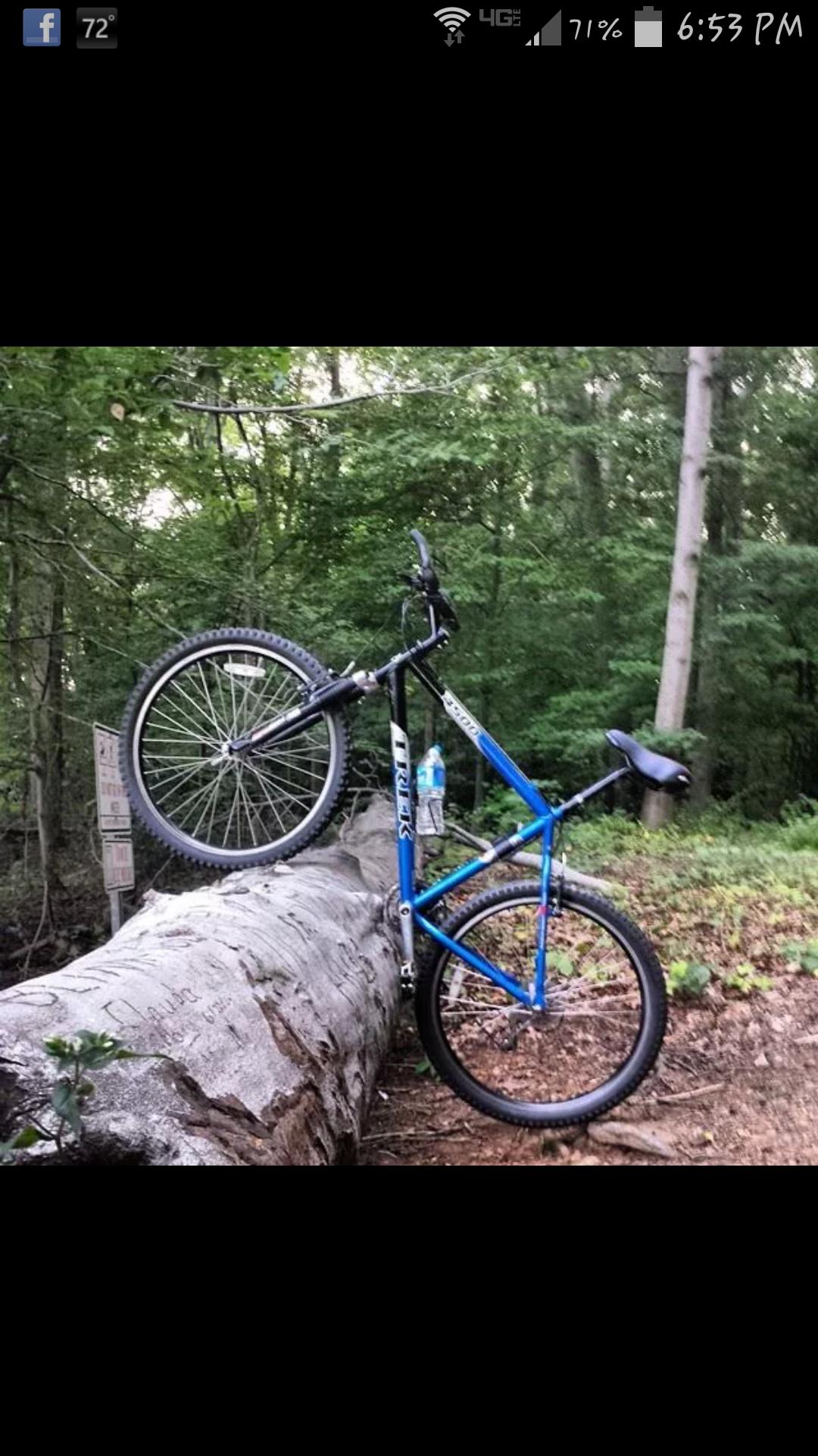 Trek 4500: A blue bicycle leaning against a fallen log in a forested area, with one wheel elevated off the ground. In the background, there are trees and a water bottle resting on the log.