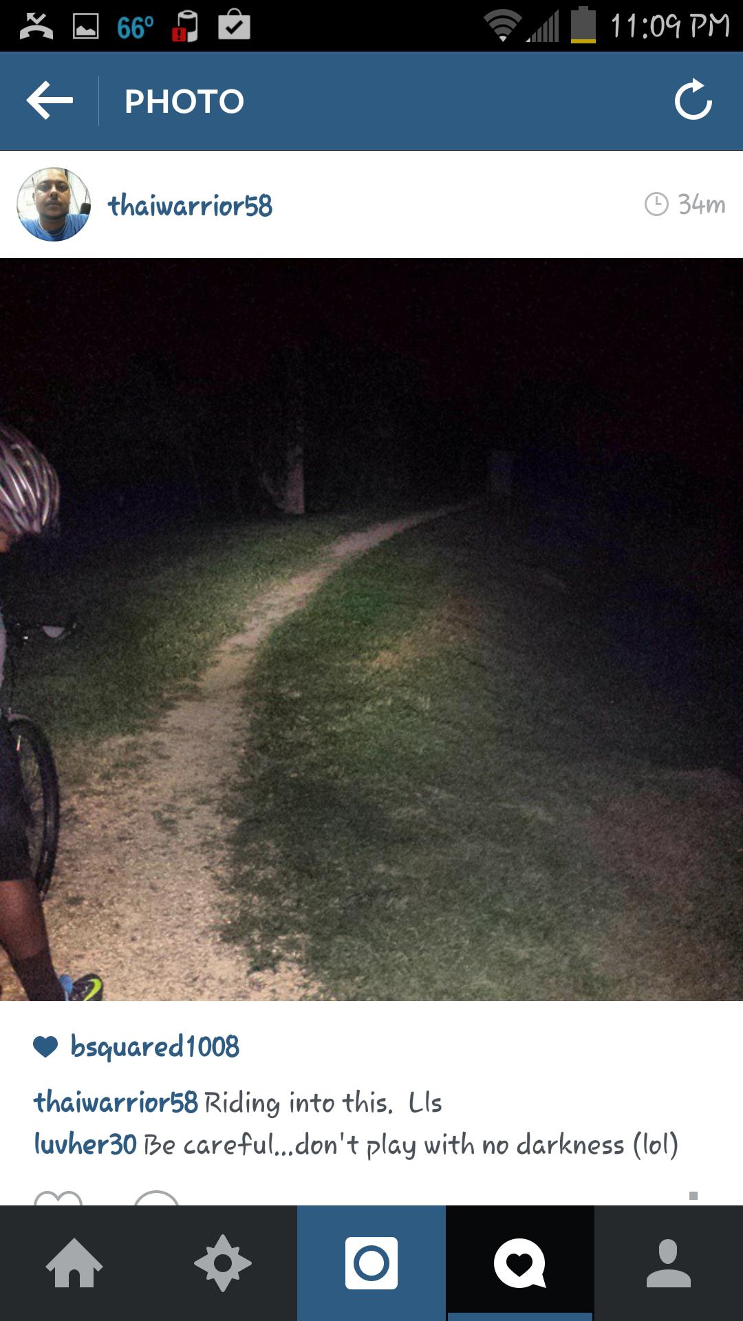 A dimly lit gravel path winding through grass, with a cyclist in the foreground wearing a helmet. The scene appears dark, suggesting it is night, and the cyclist seems to be preparing to ride. C&O Canal mountain bike trail.