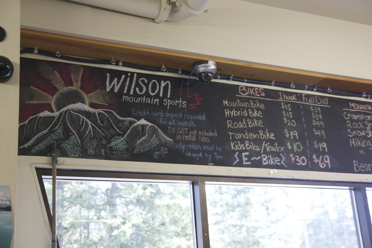 Chalkboard menu displaying bike rental rates at Wilson Mountain Sports, featuring options for mountain bikes, hybrid bikes, road bikes, tandem bikes, and children