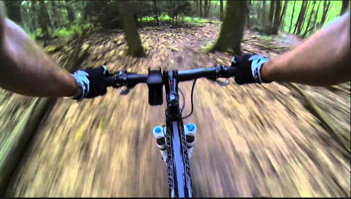 A close-up view of mountain bike handlebars with hands gripping them, surrounded by a blurred forest landscape while biking down a trail covered with fallen leaves. The image captures a sense of speed and adventure in a natural setting. Swatara State Park mountain bike trail.