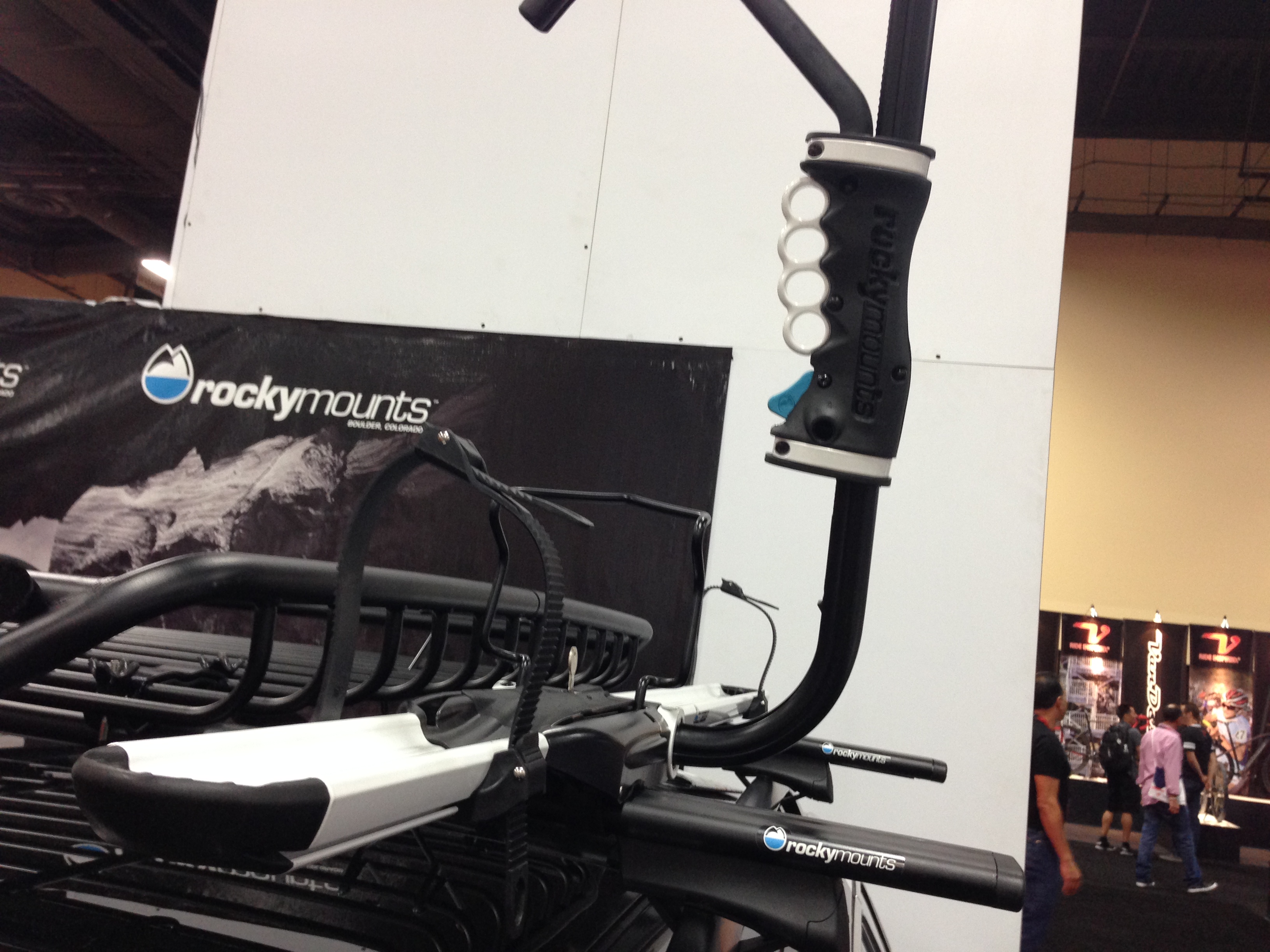 A close-up view of a RockyMounts bike rack showcasing its adjustable arm and mounting features. The background includes a partial display with the RockyMounts logo, highlighting the product's branding.
