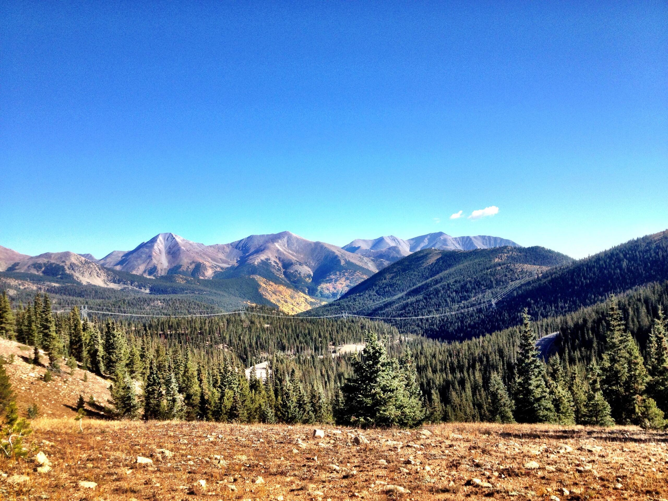 Beautiful mountain landscape featuring rolling hills and peaks beneath a clear blue sky. Pine trees cover the foreground with rocky terrain, highlighting the natural beauty of the wilderness. CDT: Monarch Pass to Boss Lake / Hunt Lake Trail mountain bike trail.
