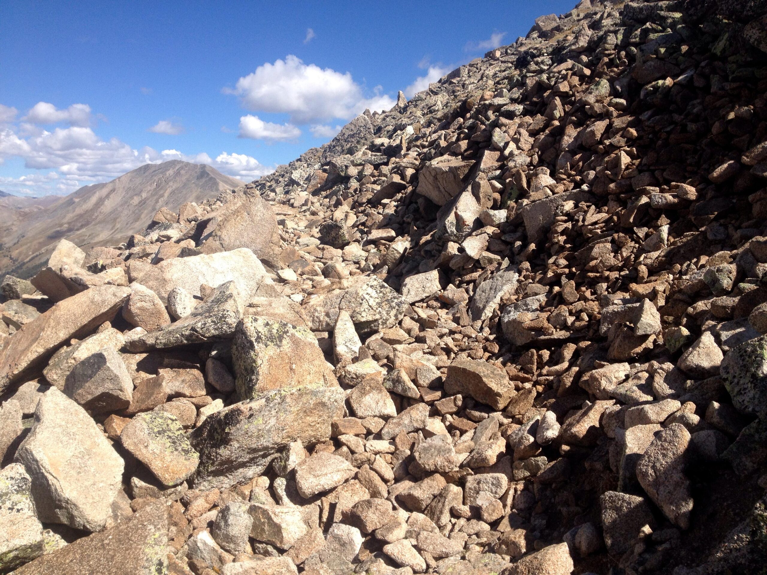 Rocky terrain strewn with various sizes of boulders and stones, set against a backdrop of blue sky and distant mountains. The scene captures a natural environment typical of high-altitude landscapes. CDT: Monarch Pass to Boss Lake / Hunt Lake Trail mountain bike trail.
