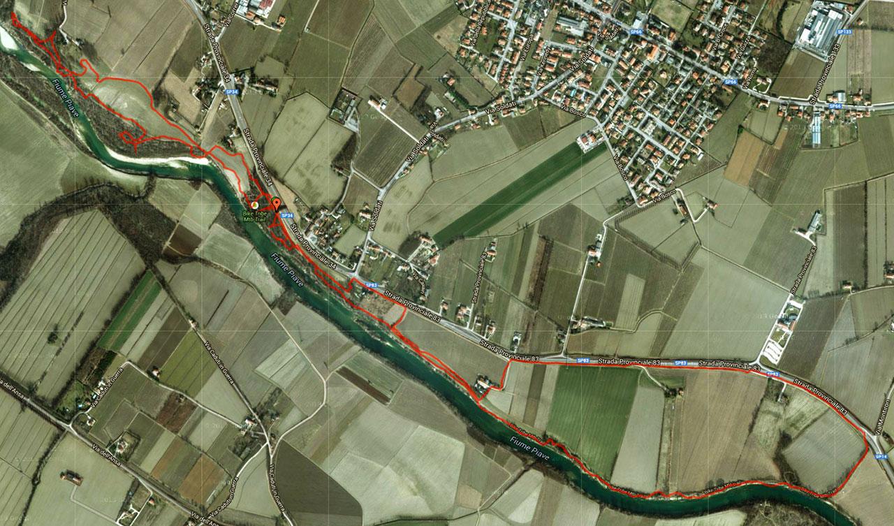 A detailed aerial map showing the course of a river surrounded by farmland and residential areas. The route is highlighted in red, indicating a walking or biking trail alongside the river, with labeled roads and notable points of interest marked along the path. The map captures a landscape of fields, waterways, and nearby settlements. Bike Tribe Mtb Trail mountain bike trail.