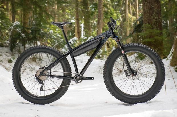 Rocky Mountain Blizzard: A black fat bike standing on snow-covered ground in a forest, surrounded by tall trees. The bike features wide tires designed for snow and rough terrain, and it has a sleek, modern design.