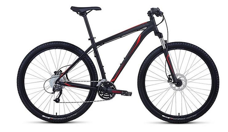 Specialized Hardrock Sport Disc 29er: A black and red mountain bike with thick tires, a straight handlebar, and a sleek frame design, positioned against a plain background. The bike features disc brakes and a multi-gear system, ideal for off-road riding.