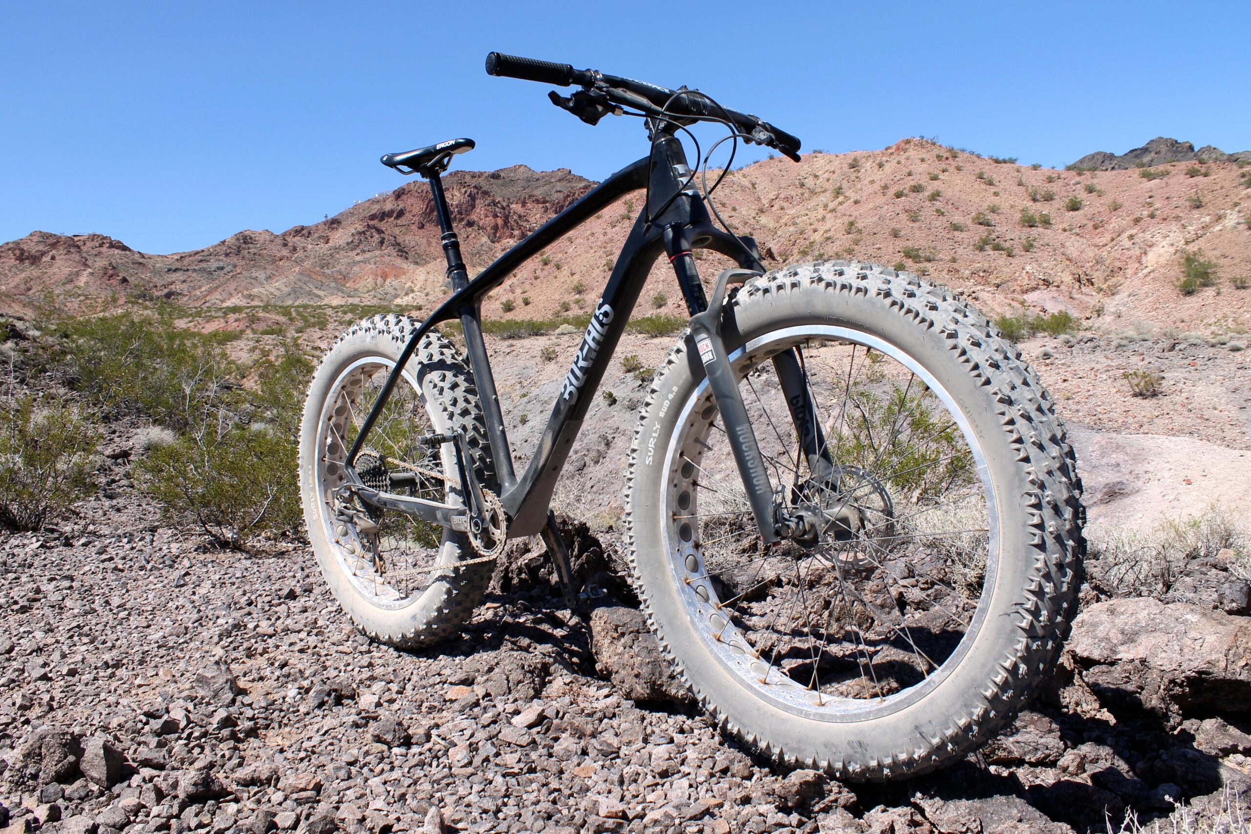 Borealis Echo: A fat tire mountain bike parked on rocky terrain with desert hills in the background under a clear blue sky.