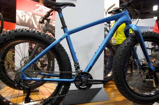 Felt Double Double: A blue fat tire mountain bike on display, featuring wide tires and a sturdy frame, set against a neutral background with other bicycles visible in the blurred backdrop. The bike is positioned to highlight its frame and gear system.