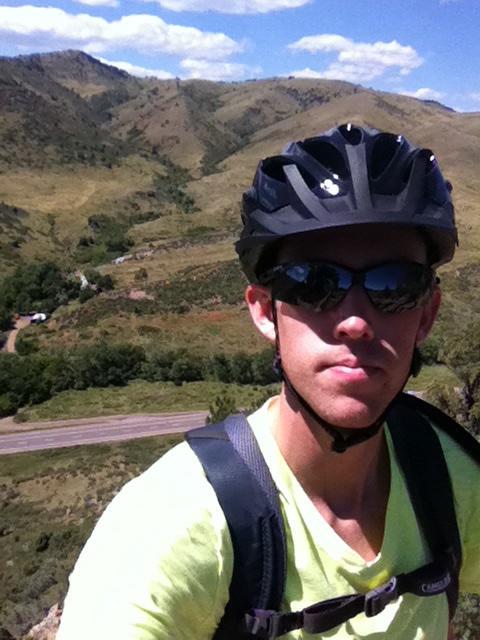 Trek 4500: A person wearing a helmet and sunglasses poses for a selfie on a mountain trail, with rolling hills and a clear blue sky in the background.