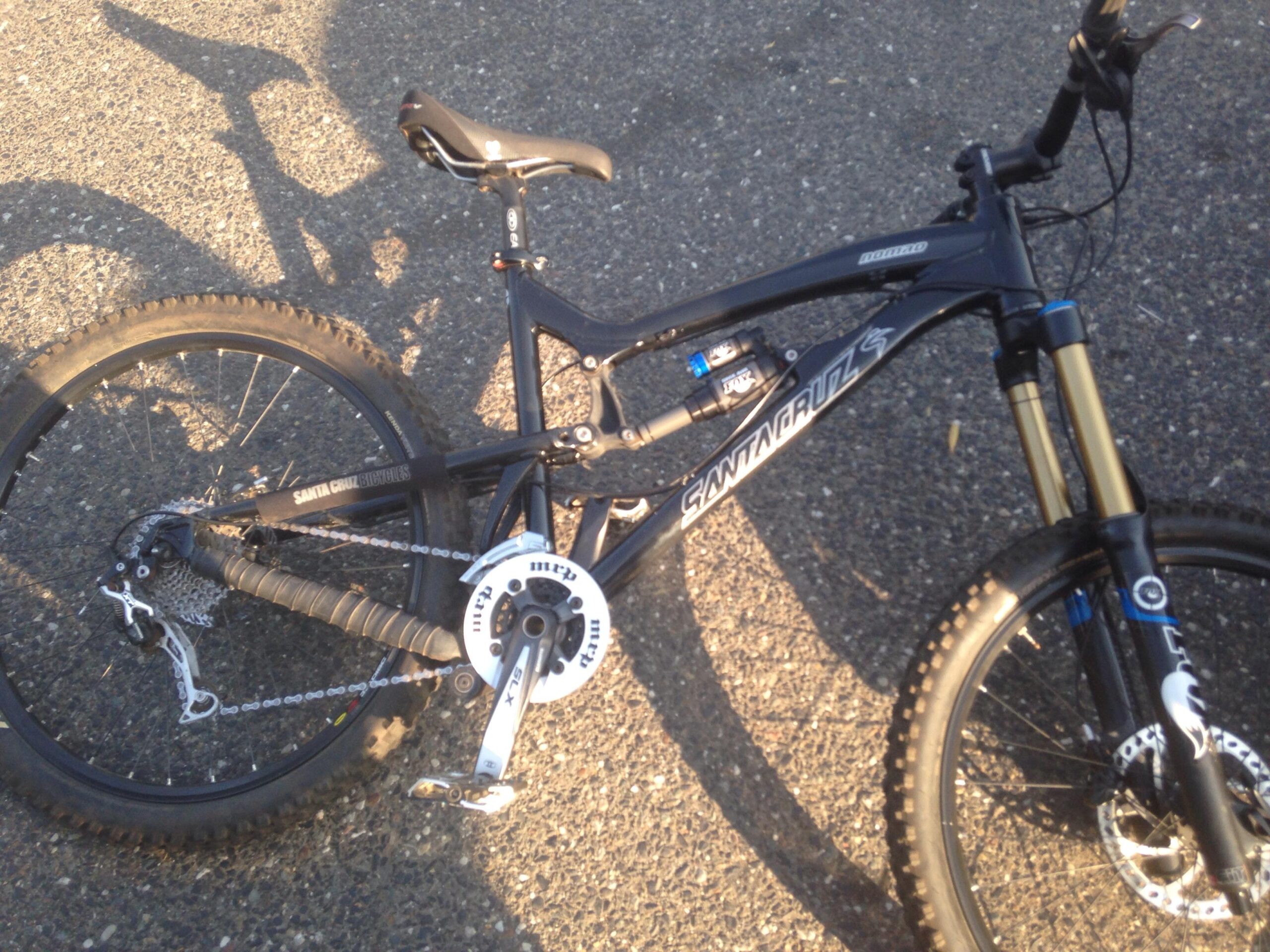 Santa Cruz Nomad: Alt text: A close-up view of a black mountain bike resting on a gravel surface, featuring a prominent brand name "Santa Cruz" on the frame, along with a well-defined suspension system and rugged tires suitable for off-road riding.