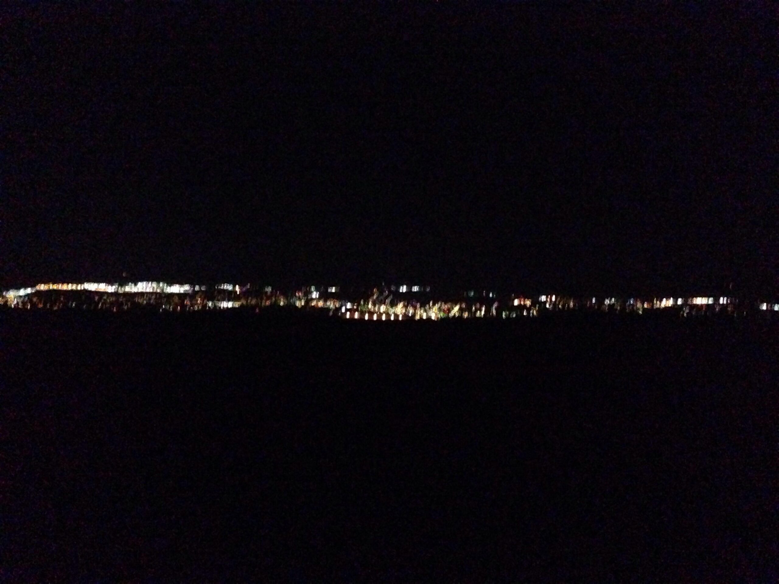 City skyline lit up at night with various lights reflecting against a dark sky. The image shows a horizon filled with a mix of bright and colorful lights. Blueberry mountain bike trail.