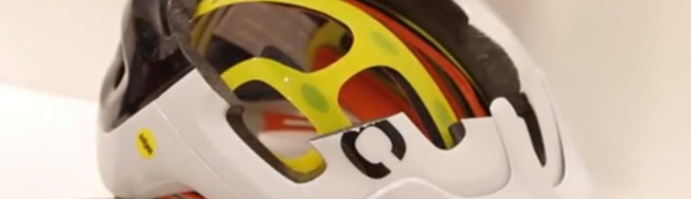 A white bicycle helmet resting on a surface, showcasing its interior design with bright yellow accents and a red and orange inner lining. The helmet features ventilation openings and a adjustable strap for a secure fit.