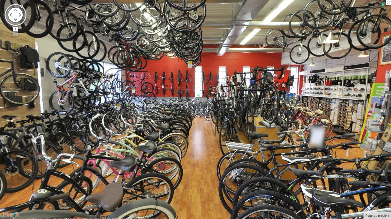 A spacious bicycle shop filled with a variety of bicycles, including road bikes, mountain bikes, and children's bikes. The interior features bike racks on the walls and a wooden floor, with bikes of different colors and styles lining the aisles. The walls are painted red, creating a vibrant atmosphere.
