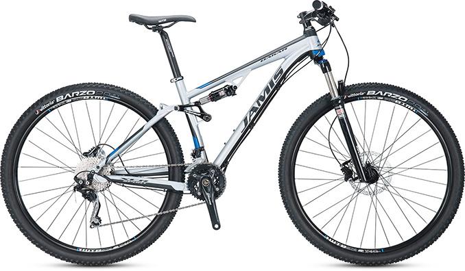 Jamis Dakar XCR Sport: A modern mountain bike with a silver frame, featuring thick tires and a front suspension fork. The bike is equipped with disc brakes and a variety of gears, designed for off-road terrain.