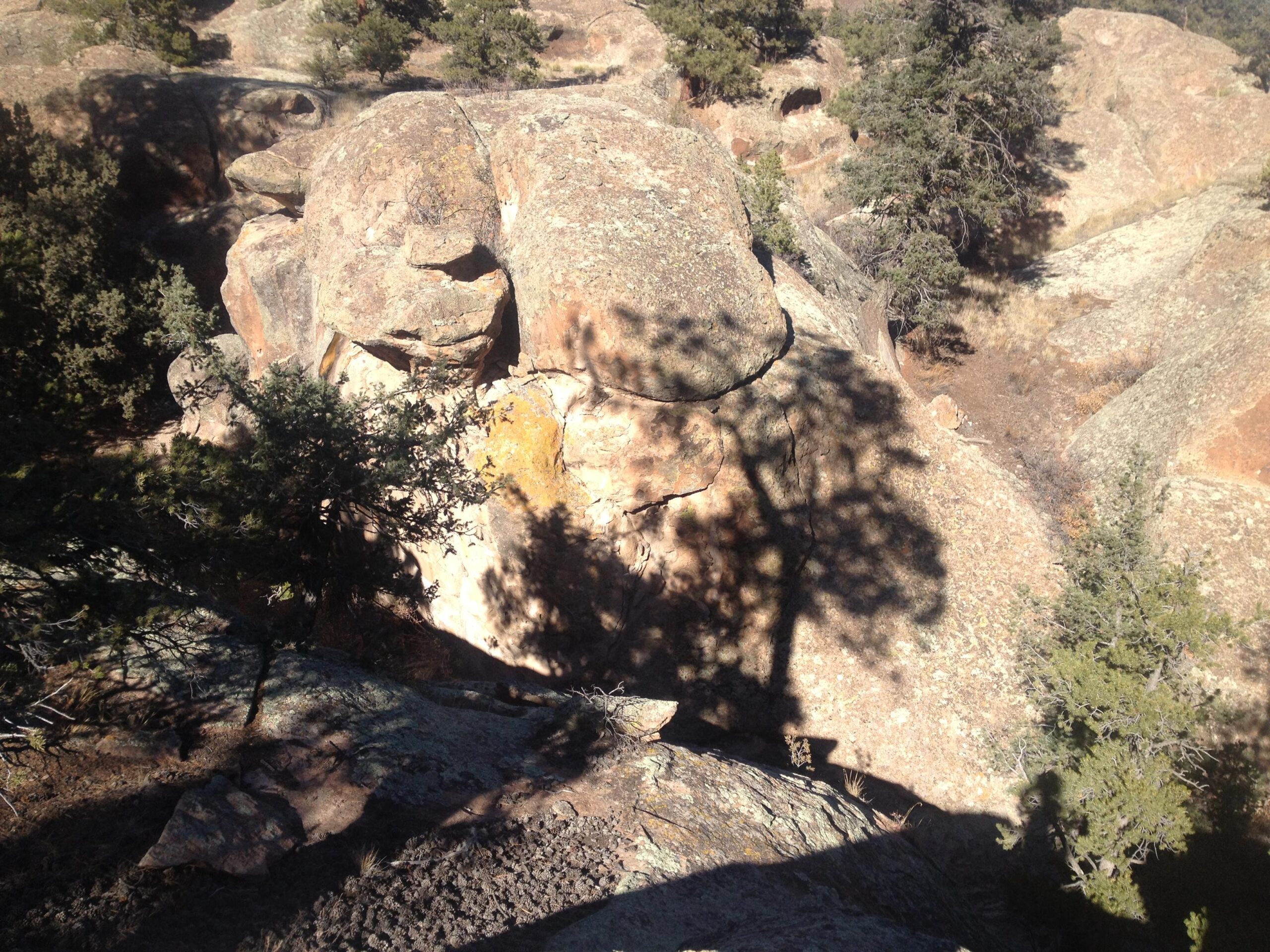 Rugged rocky landscape with large boulders and sparse vegetation, featuring the shadows of nearby trees cast on the rocky surface. The scene captures the natural beauty of the area, with different textures and colors of the stones. Penitente Canyon mountain bike trail.