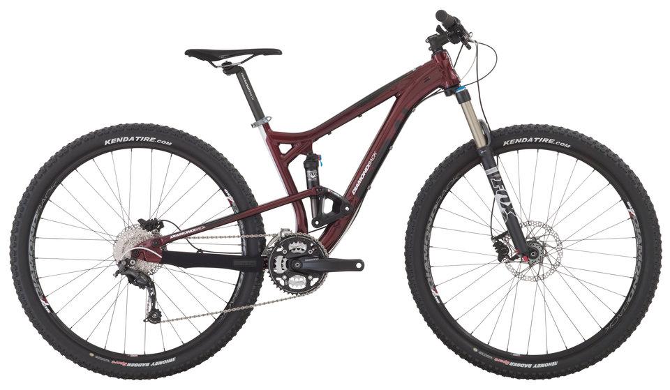 Diamondback Sortie 1: A side view of a maroon mountain bike with dual suspension, featuring wide knobby tires, disc brakes, and a lightweight frame. The bike has a modern design with a visible gear system and a prominent shock absorber on the front fork.