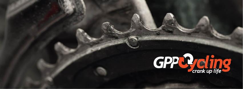 Close-up image of a bicycle chainring with visible teeth and detailing, alongside the GPP Cycling logo, which includes the slogan "crank up life." The image highlights the mechanical aspect of cycling, focusing on the components of a bike.