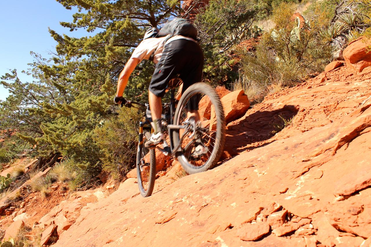 A mountain biker navigating a rocky trail surrounded by trees and blue sky, showcasing outdoor adventure and rugged terrain. Hangover mountain bike trail.
