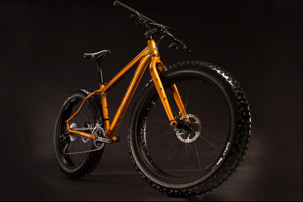 Salsa Mukluk: An orange mountain bike with thick, knobby tires, showcased against a dark background. The bike features a sturdy frame and front suspension, highlighting its design for off-road performance.