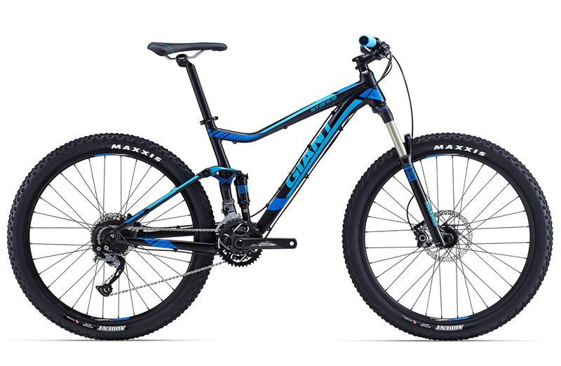 Giant Giant Stance 2: A blue and black mountain bike featuring a lightweight frame, front suspension, and rugged tires. The bike is positioned at an angle with a focus on its components, including the disc brakes and gearing system. The brand name "Giant" is prominently displayed on the frame.