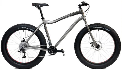 Motobecane Boris X5: A silver fat tire mountain bike with wide tires, featuring a sleek frame, adjustable handlebars, and a disc brake system. The bike is positioned against a plain background to highlight its design.