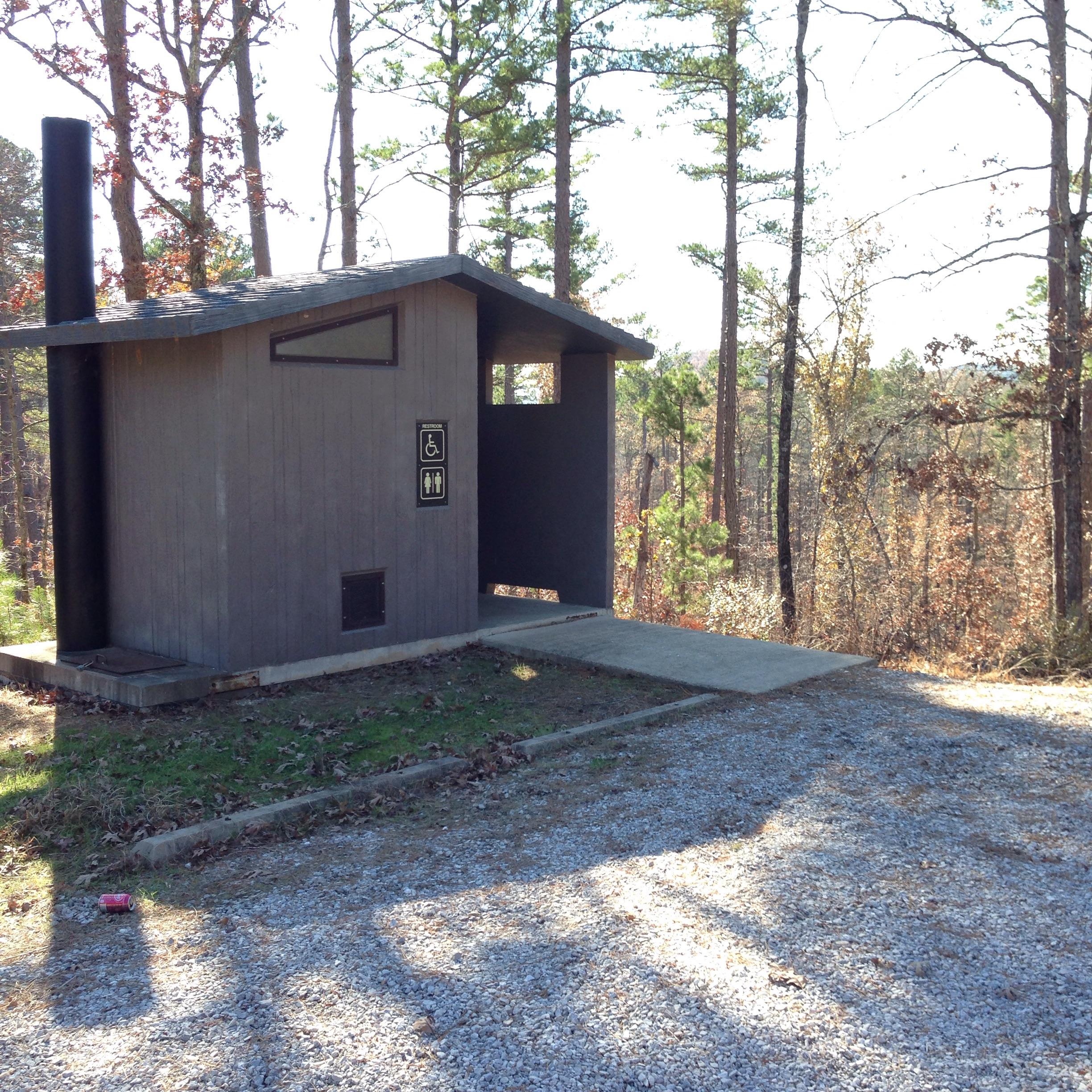 Outdoor restroom facility with signage for men, women, and accessible use, surrounded by trees in a natural setting. Syllamo Trails mountain bike trail.