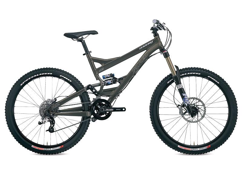 Specialized Enduro Pro: Mountain bike with a grey frame, wide tires, and front suspension. The bike features a contemporary design, suitable for off-road terrains. It has disc brakes and a gear system visible on the bottom bracket.