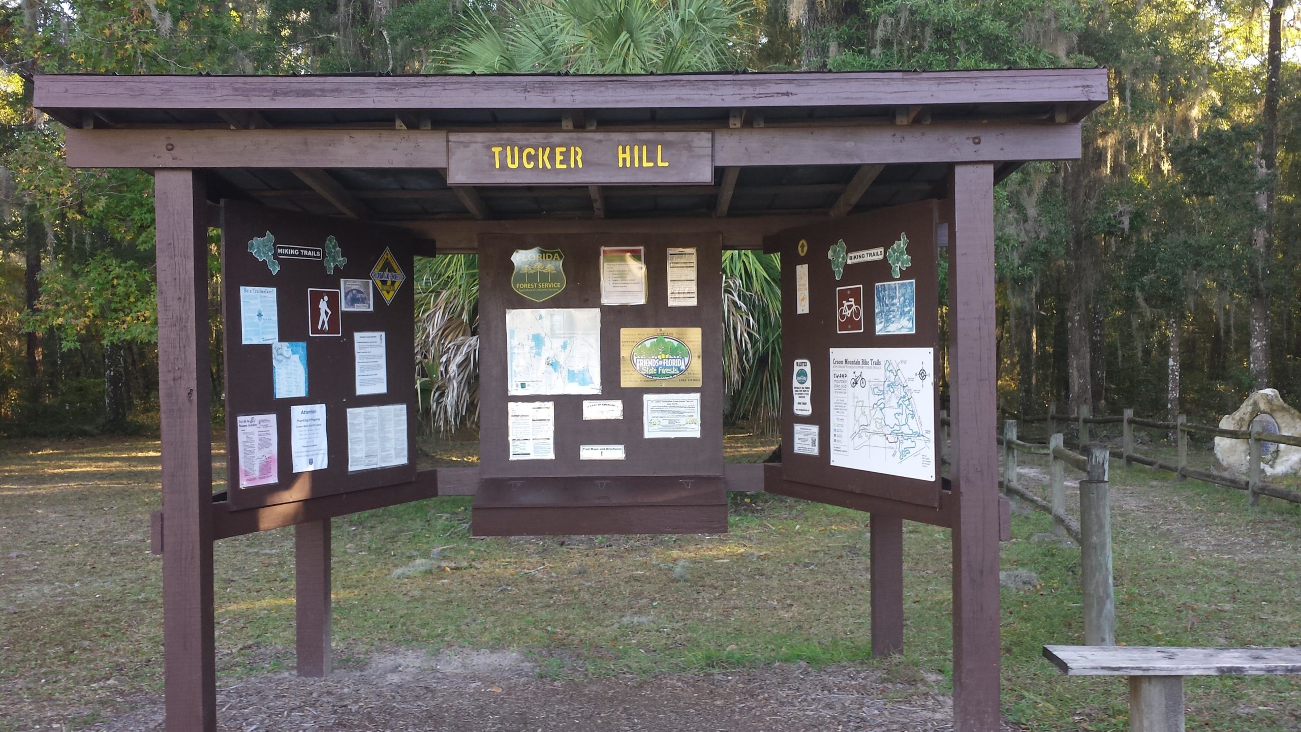 Information kiosk at Tucker Hill displaying maps and signage related to hiking trails, surrounded by trees and natural scenery. Withlacoochee State Forest: Croom Section mountain bike trail.