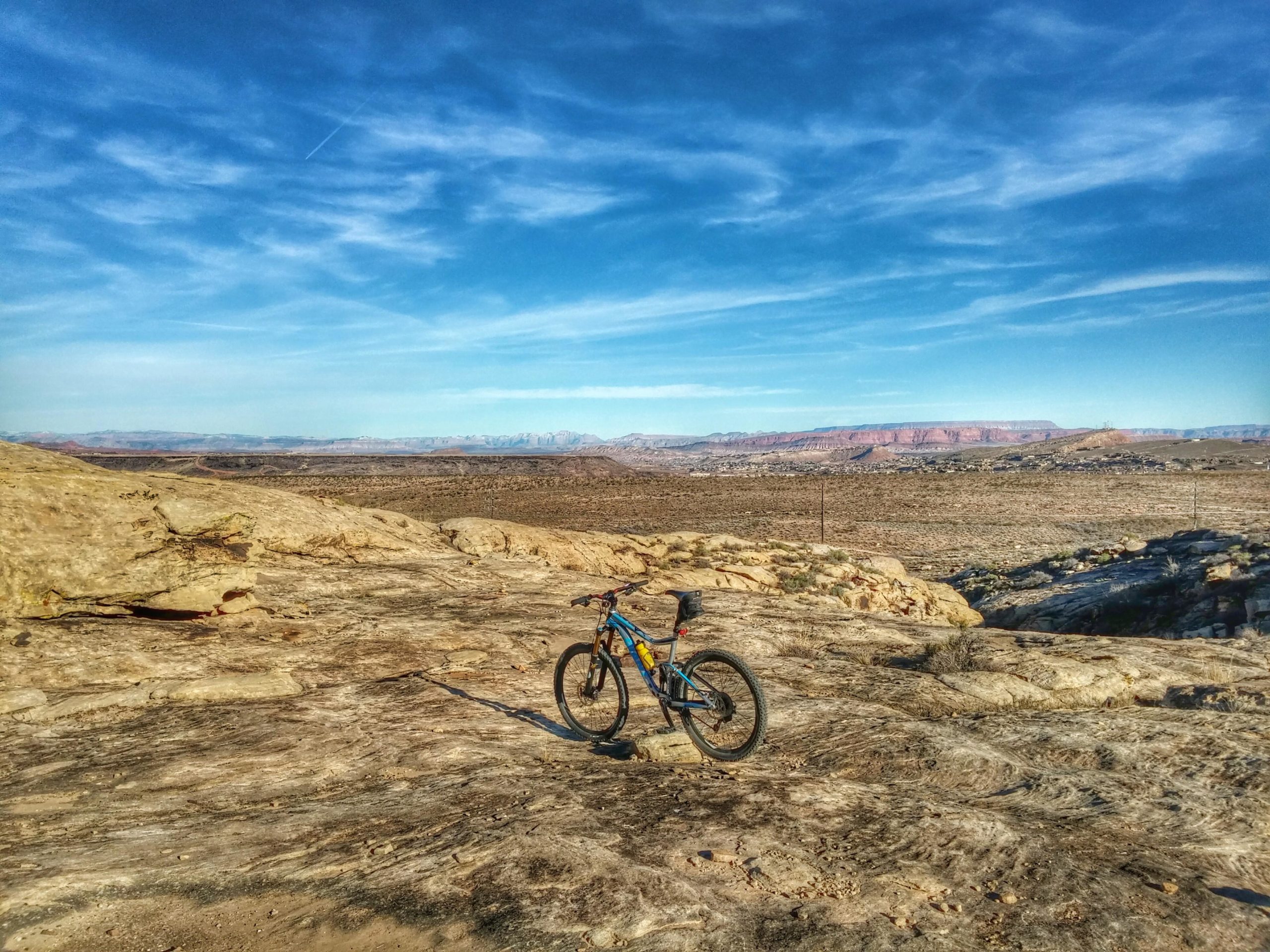 A mountain bike positioned on rocky terrain, with expansive desert landscape and distant mountains under a clear blue sky. Zen Trail mountain bike trail.