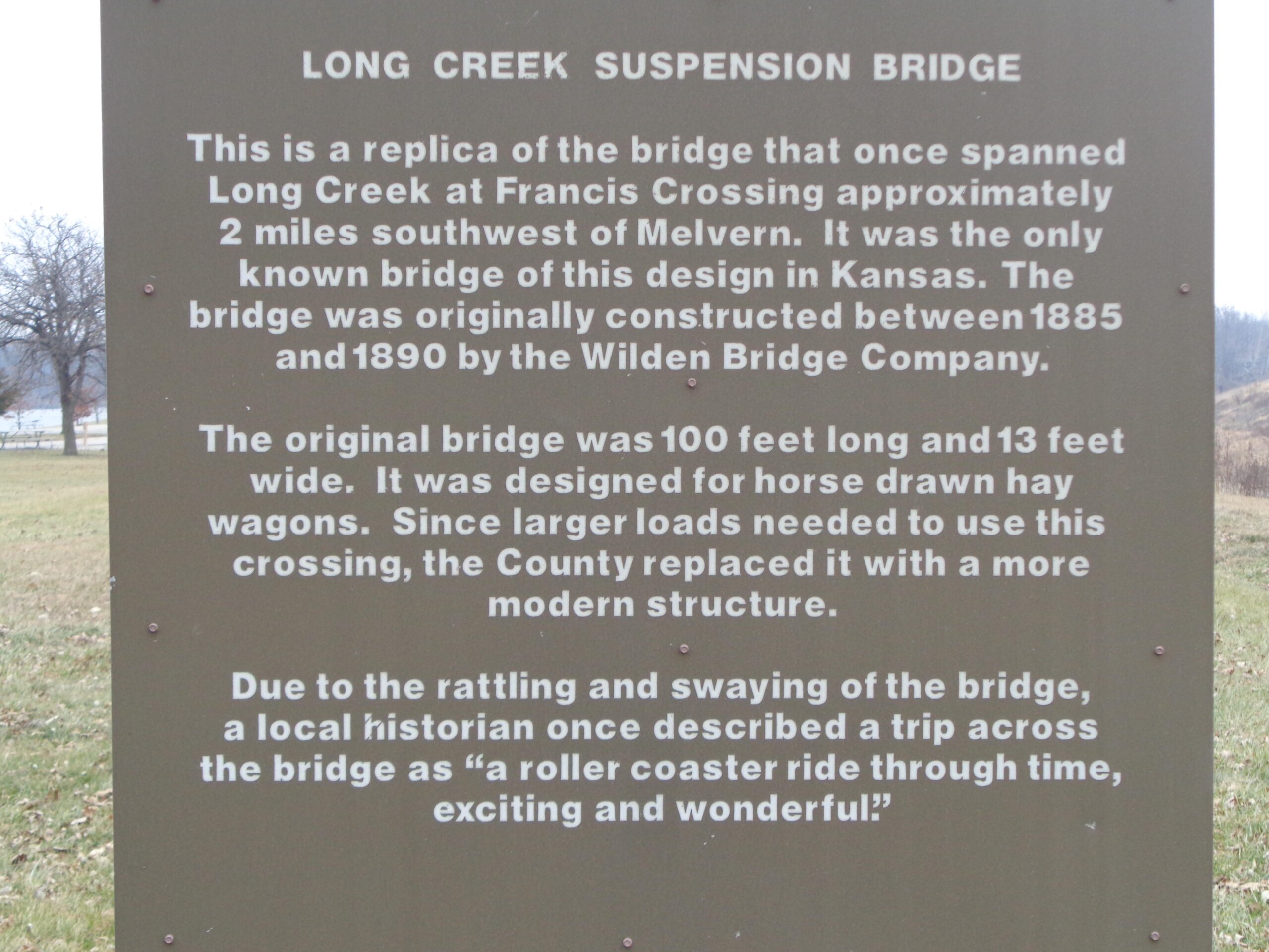 Sign describing the Long Creek Suspension Bridge, a replica of the original bridge that spanned Long Creek at Francis Crossing, Kansas. The sign includes historical information about the bridge