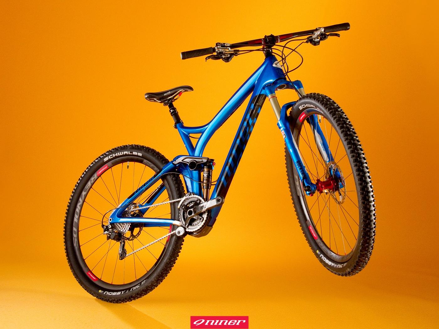 Niner R.I.P. 9 RDO: A blue mountain bike displayed against a bright orange background, featuring a sleek design, wide tires with "Schwalbe" branding, and a prominent suspension system. The bike is positioned to emphasize its frame and components, showcasing its suitability for off-road riding. A logo from the brand "Niner" is visible at the bottom of the image.
